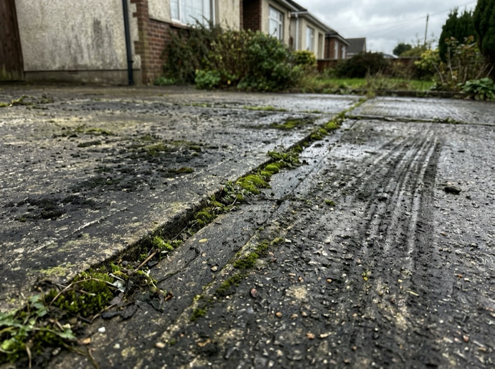 Dirty weathered concrete driveway covered in black mould and algae before pressure washing